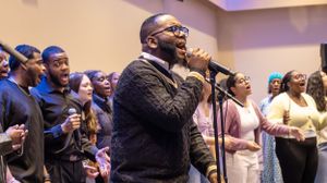 A gospel choir performer leads worship while singing into a microphone during a church service.