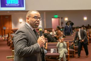 Speaker presenting to an audience in a church or conference setting with projection screen.