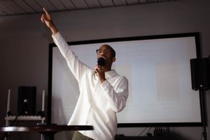 Silhouetted figure in white clothing against dramatic window lighting in a dark room.