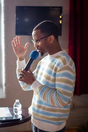 Speaker in striped sweater gestures while holding microphone during presentation.