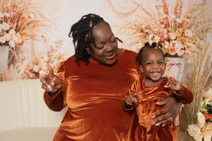 Two people in matching orange outfits embrace and smile in front of floral backdrop.