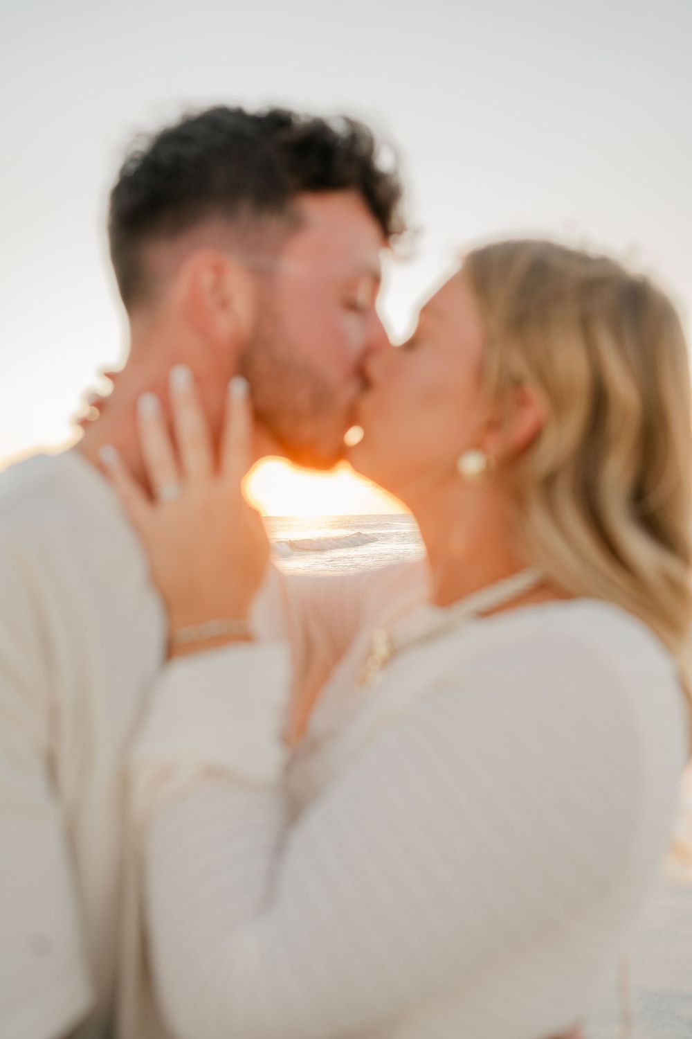 An intimate sunset kiss captured in soft focus on the beach.