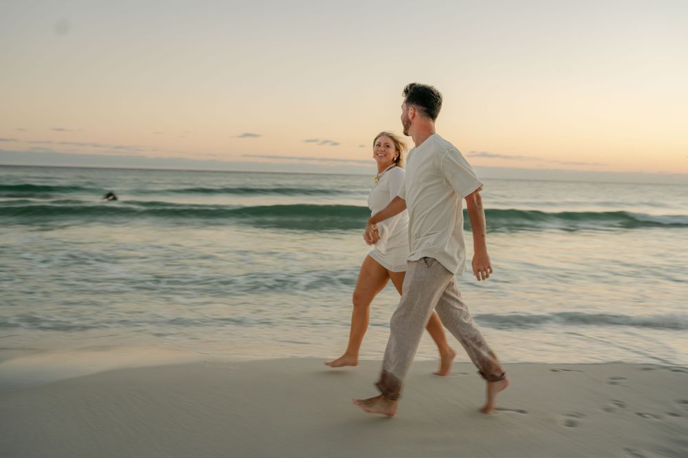 Carefree couple running and playing together on a sandy beach at golden hour.