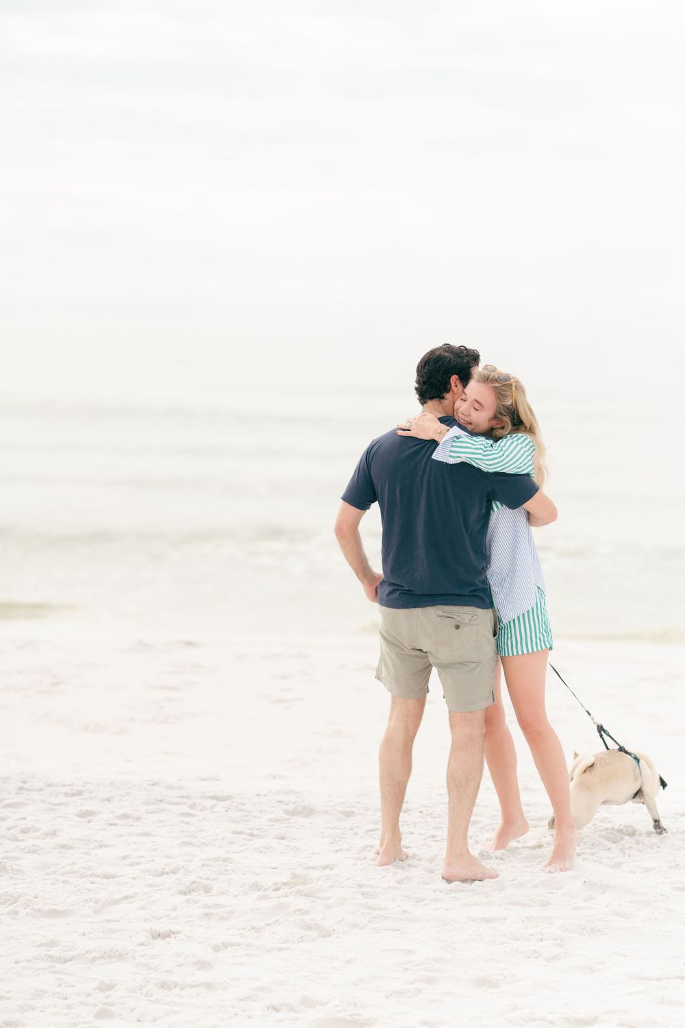 A tender embrace on the beach while walking a dog during a proposal photoshoot.