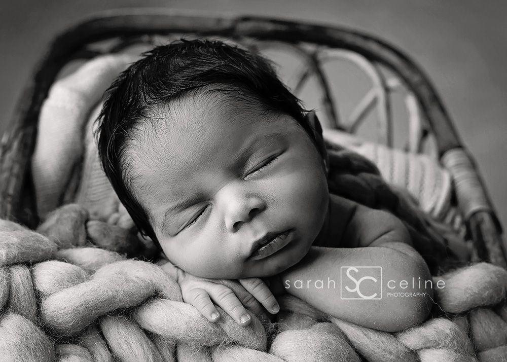 Black and white photo of sleeping newborn baby resting on chunky knit blanket.