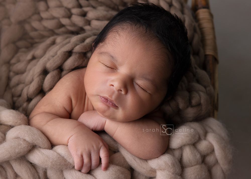 A peaceful sleeping newborn resting on a soft chunky knit blanket in neutral beige tones during a professional photo session.