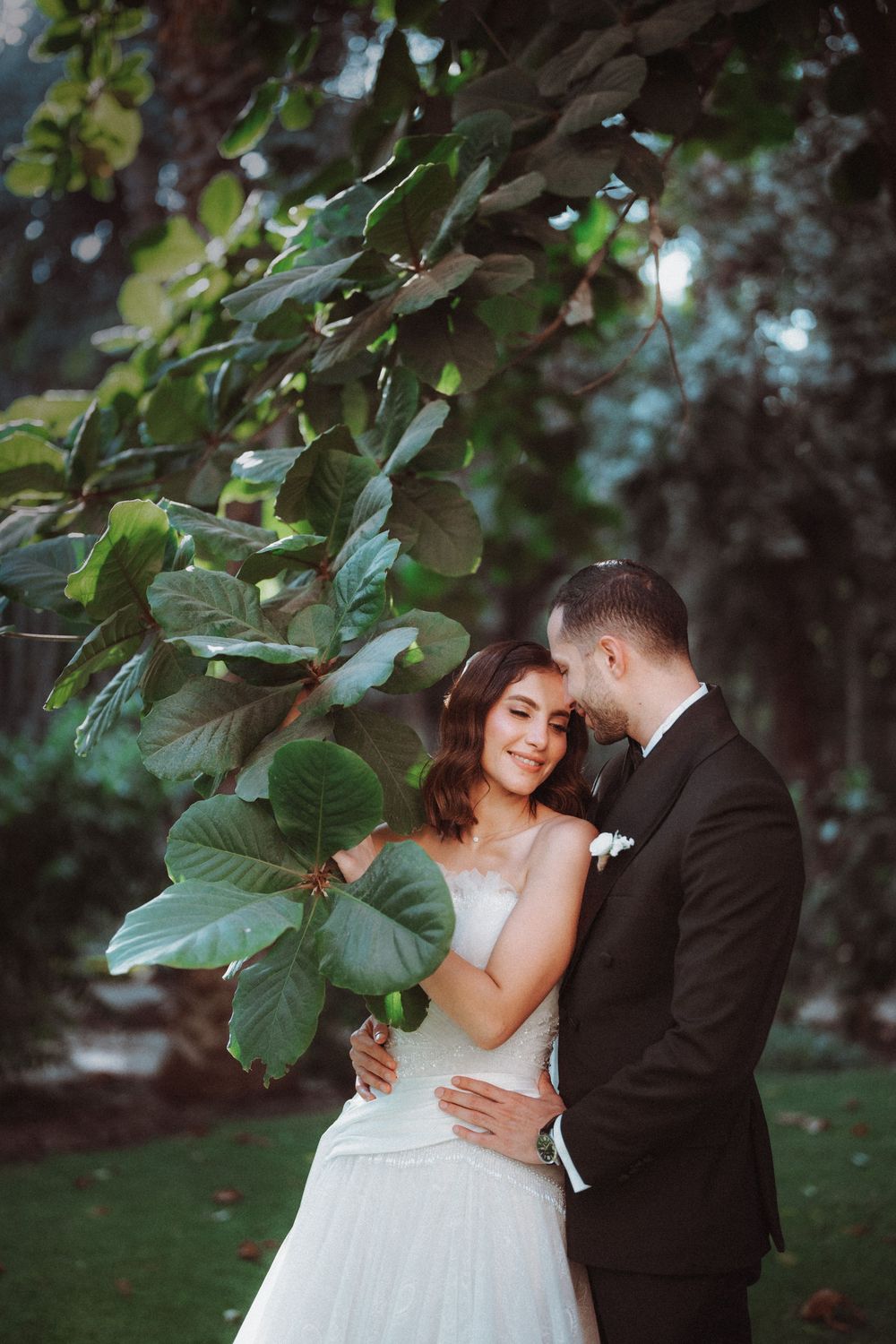 Romantic garden wedding portrait under lush green trees with natural lighting.