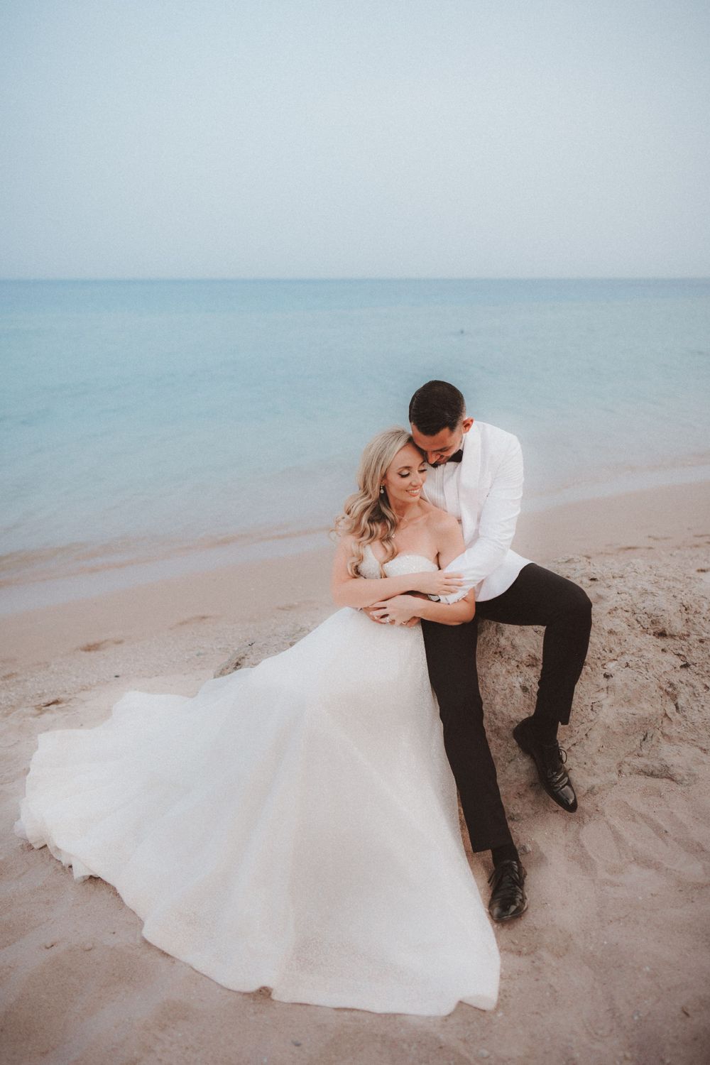 Romantic beach wedding portrait with couple lounging on sandy shore at dusk.