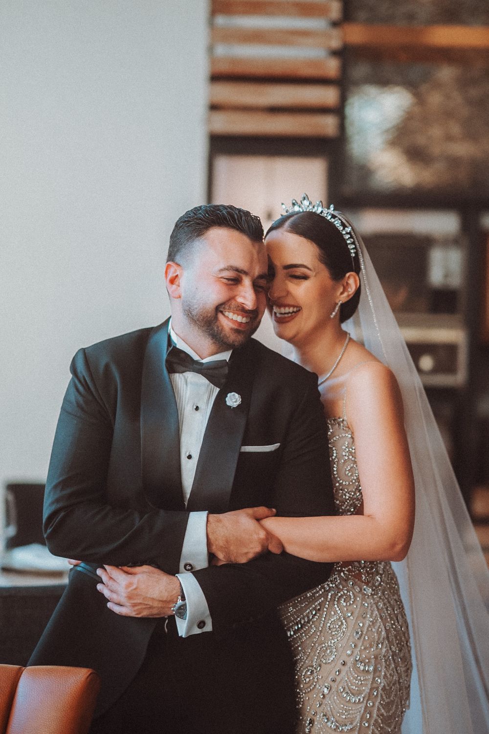 A happy couple shares a joyful moment together on their wedding day, wearing formal attire and a bridal veil.