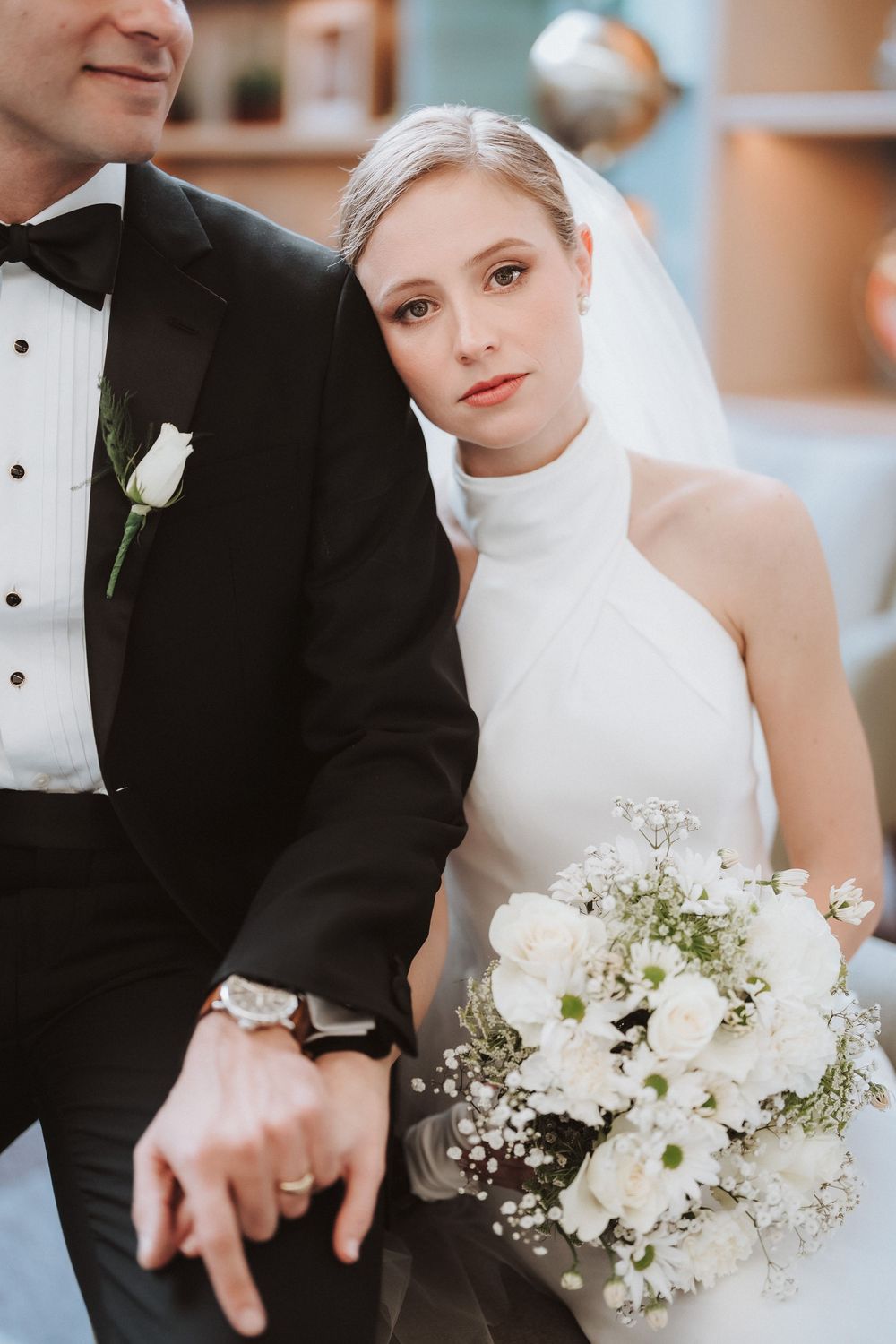 Elegant wedding portrait featuring a high-neck white bridal gown, black tuxedo, and delicate white floral bouquet.