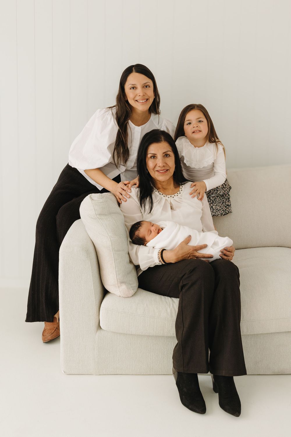 A series of four minimalist family portraits on a white couch showing tender moments between mother and newborn baby.
