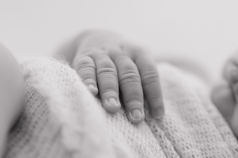 Close-up black and white image of baby hands grasping soft knitted fabric.