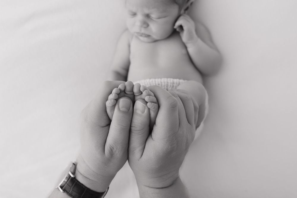 A series of black and white close-up photos showing tiny baby feet and hands in various gentle poses.