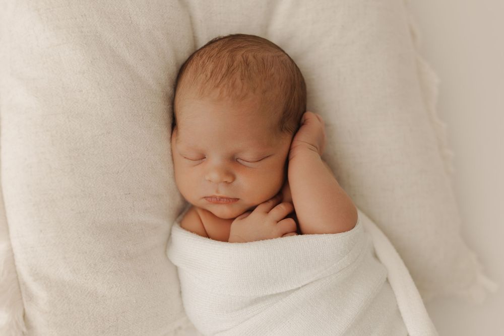 Newborn baby sleeping peacefully on soft white bedding in a series of close-up shots.
