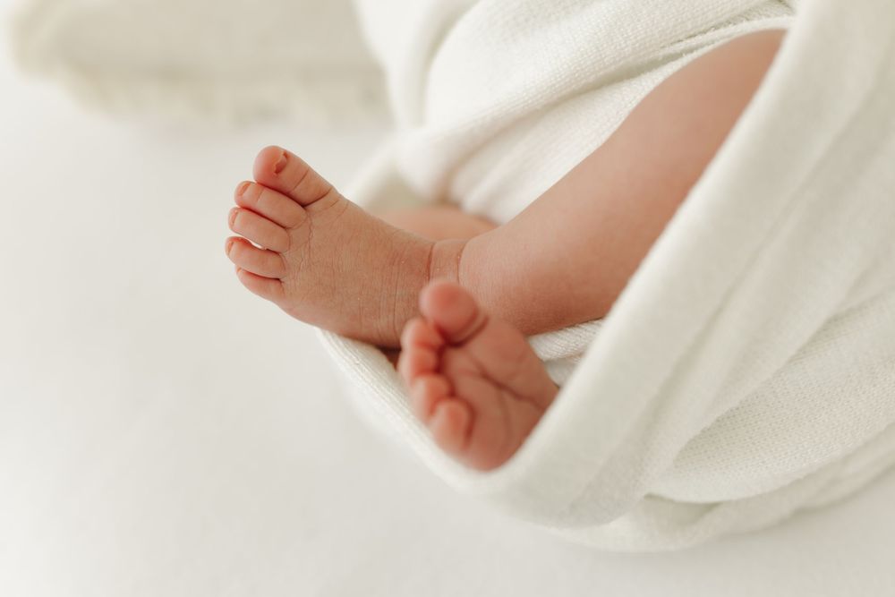 Close up view of tiny newborn baby feet wrapped in soft white blanket against light background.