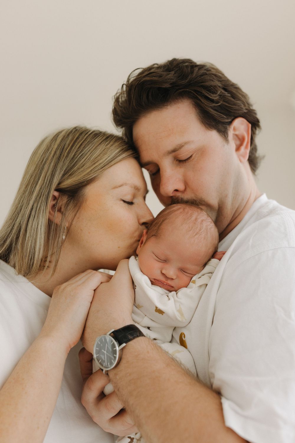 A series of intimate photos showing tender moments between parents and their sleeping newborn baby in soft lighting.