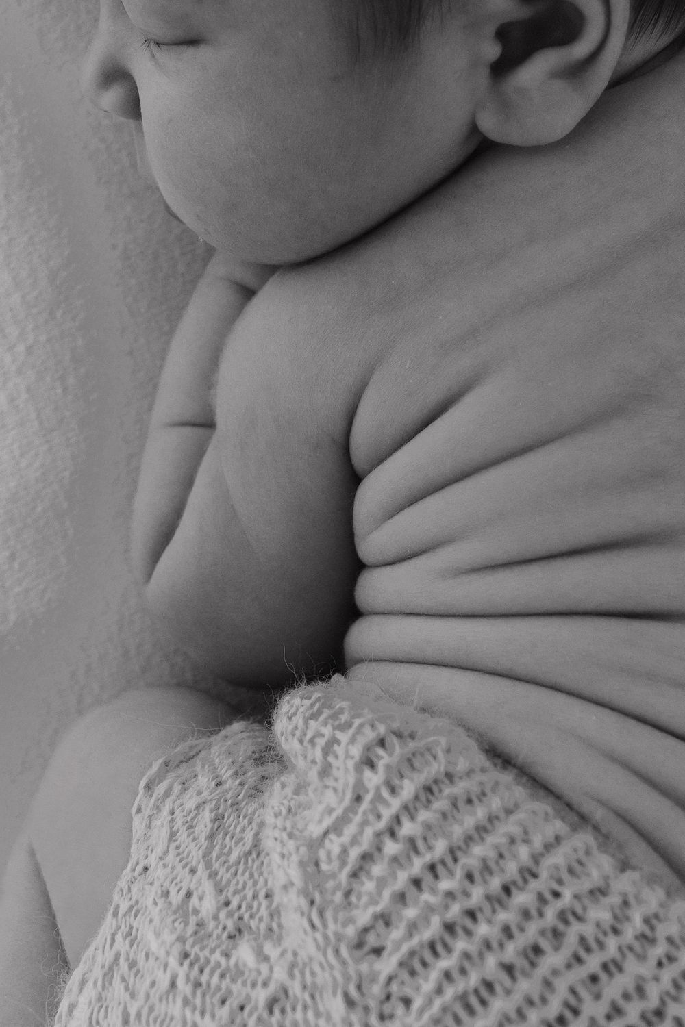A close-up black and white photo showing a baby wearing a knitted blanket while sleeping.