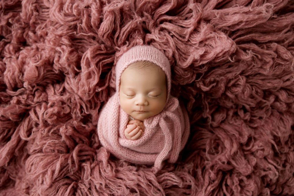 Newborn baby girl in a potato sack pose, mauve flokati set up.