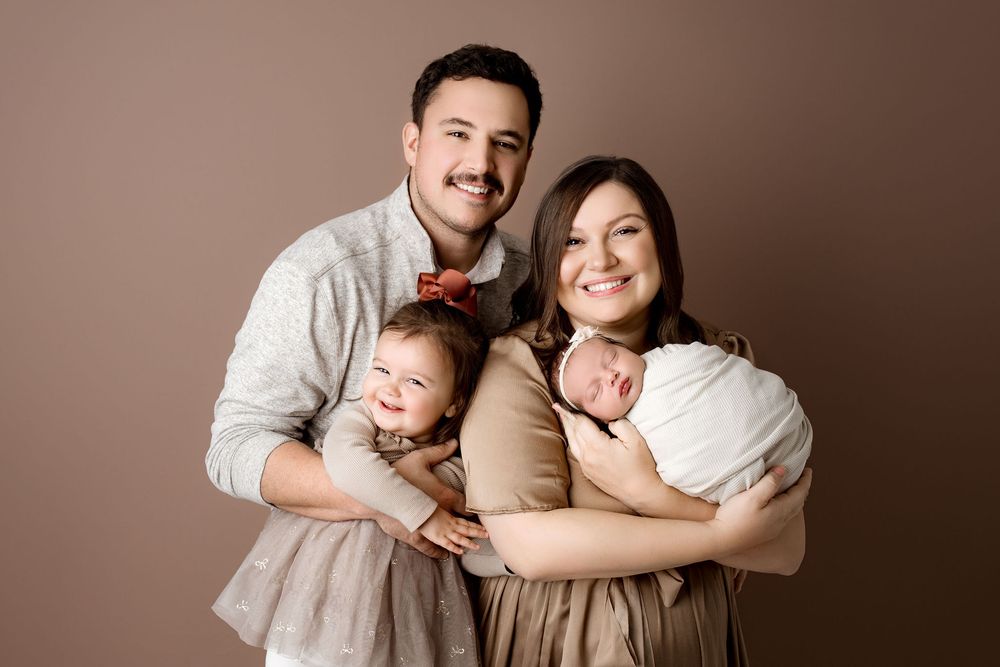 Newborn family portrait of a family of four. Toddler big sister smiling
