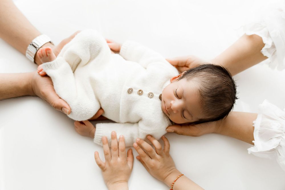 Newborn baby boy in a white knitted romper surrounded by his parent's and big brothers hands. The "you're never alone" kind of message