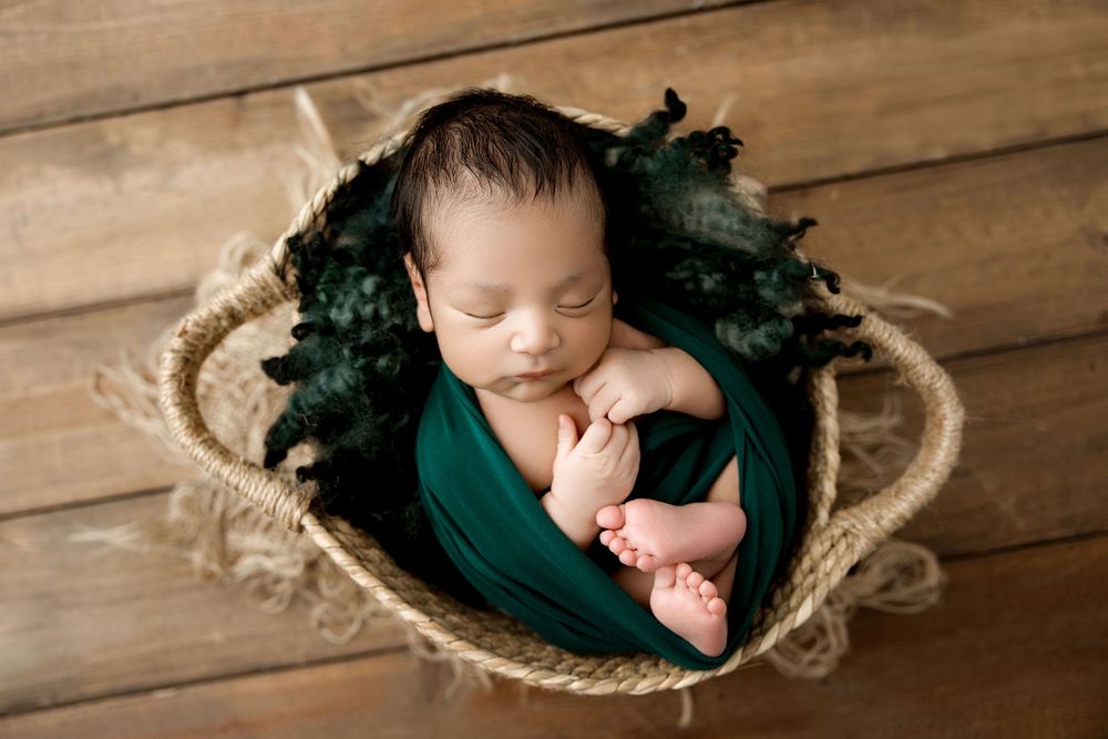 Sleeping newborn baby wrapped in an emerald green wrap and placed in a basket