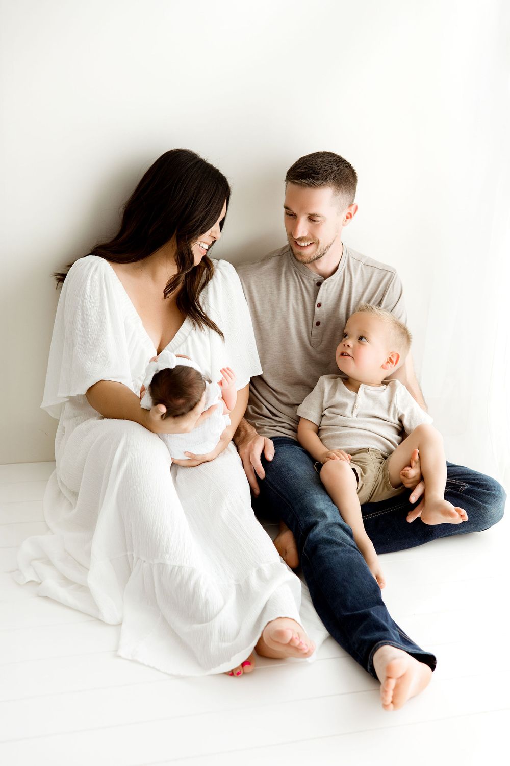 Family in a candid moment looking at each other, sitting by the wall. Mom is holding a newborn baby girl. Barrington IL newborn sessions