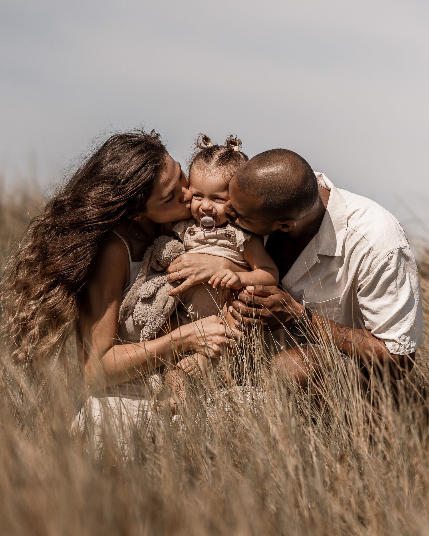 A tender family moment captured in tall grass during golden hour.