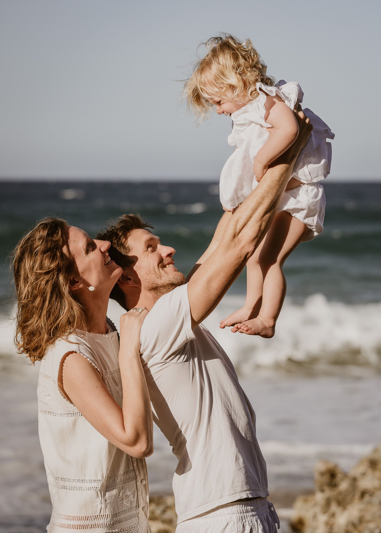 A joyful family moment at the beach with a child being lifted high in the air.