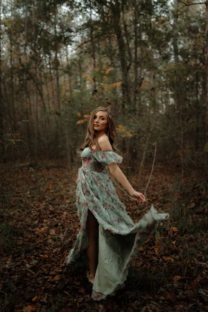 A figure in a flowing mint green dress twirls gracefully through a moody autumn forest setting.