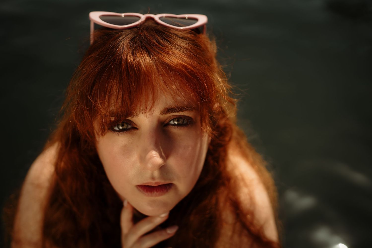 Close-up portrait of someone with vibrant red hair and sunglasses perched on their head.