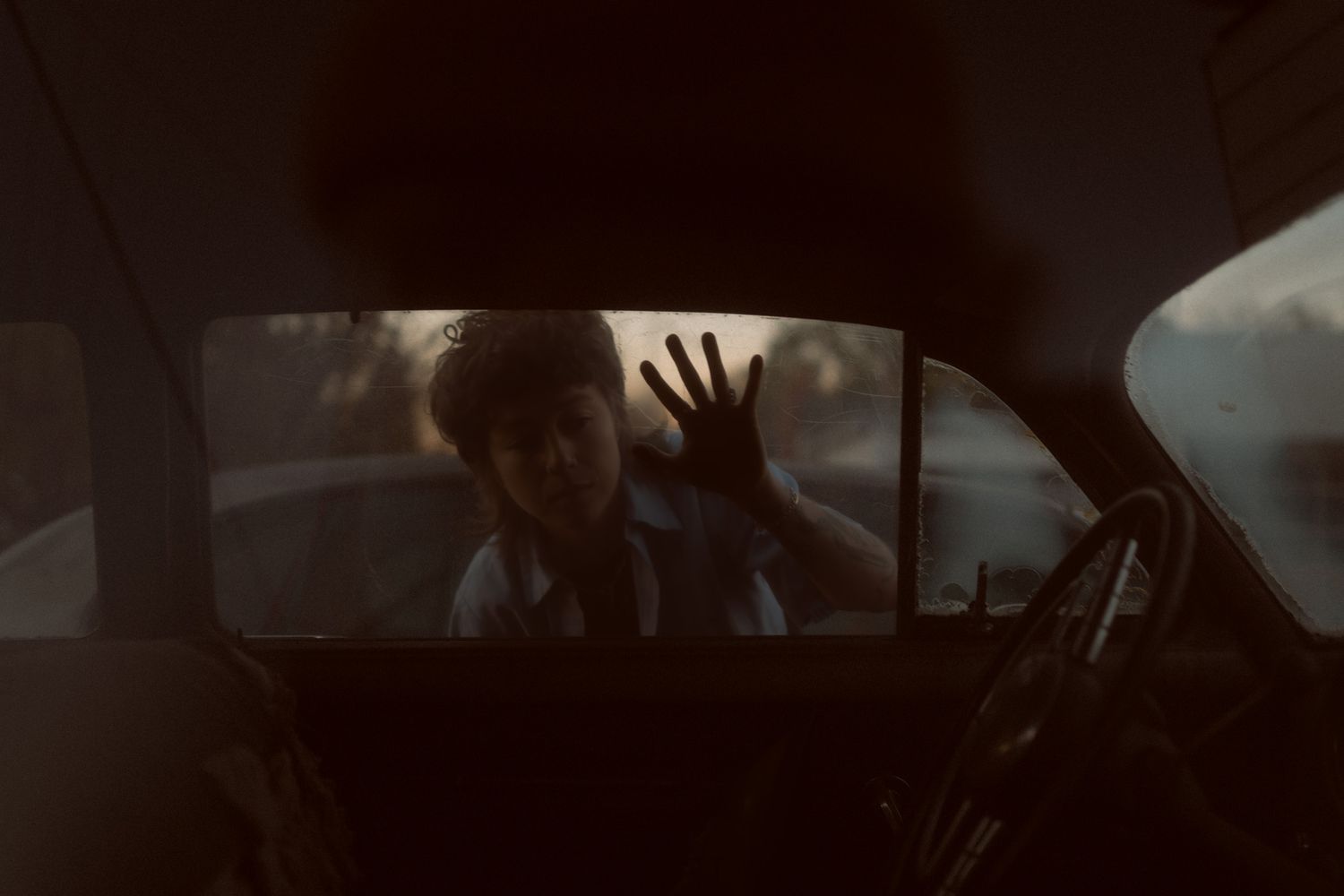 Child pressing hand against rain-streaked car window, viewed from inside dark vehicle interior.