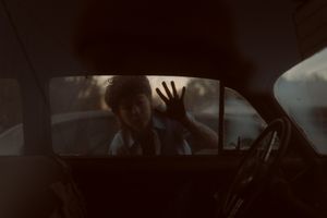 Child pressing hand against rain-streaked car window, viewed from inside dark vehicle interior.