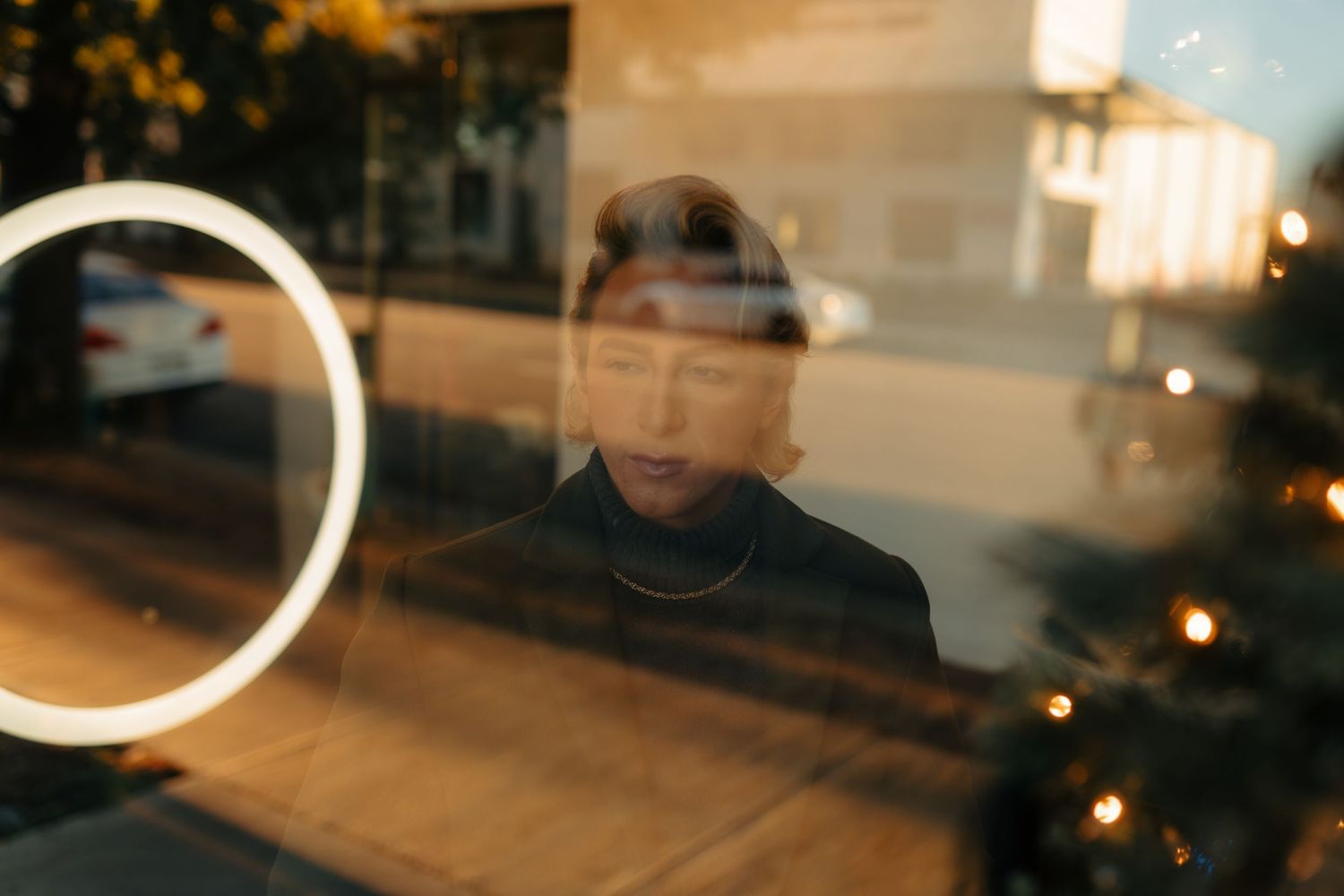 Artistic reflection portrait through glass with circular light element and evening ambiance.