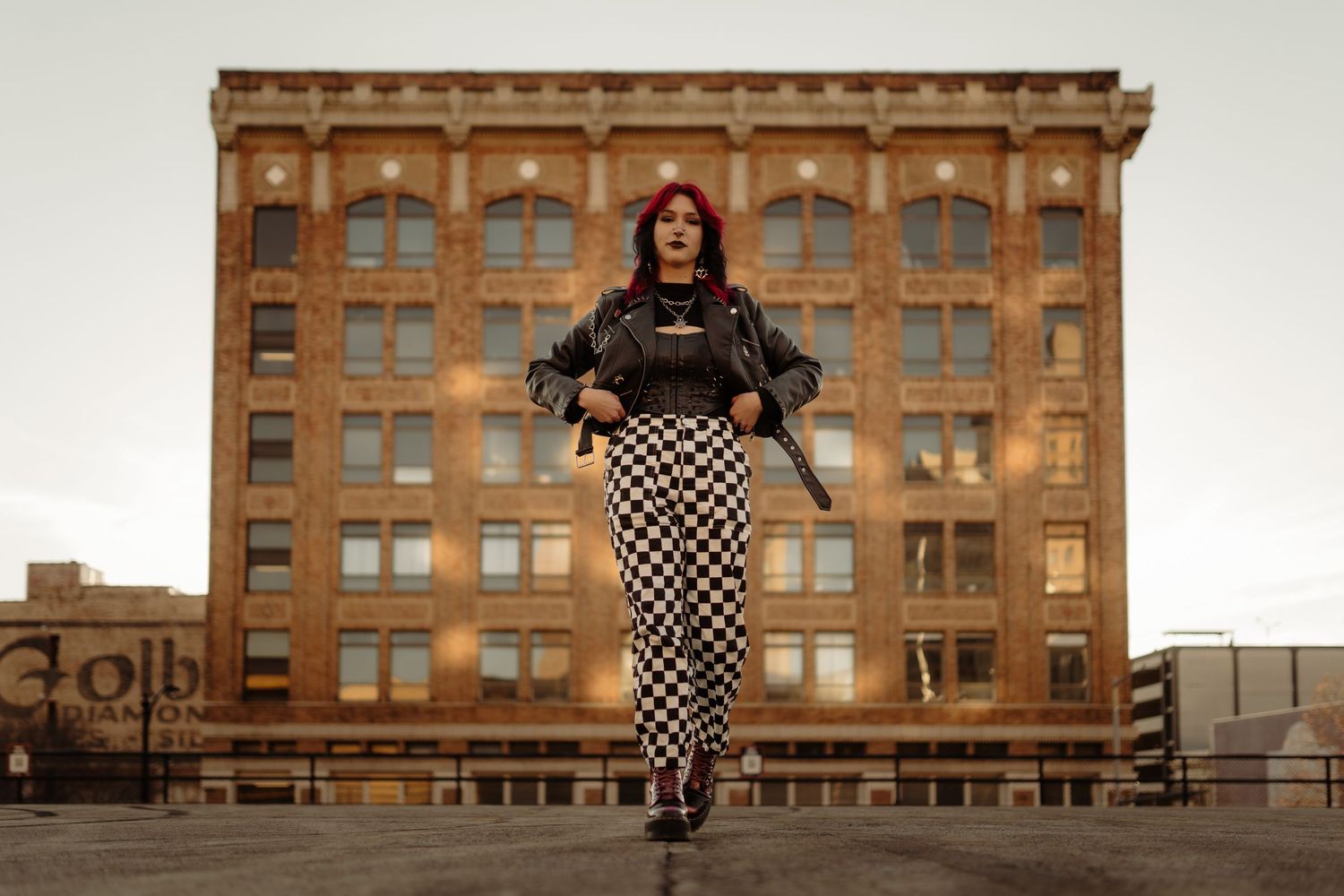 A person in checkered pants poses confidently in front of a historic brick building.