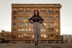 A person in checkered pants poses confidently in front of a historic brick building.