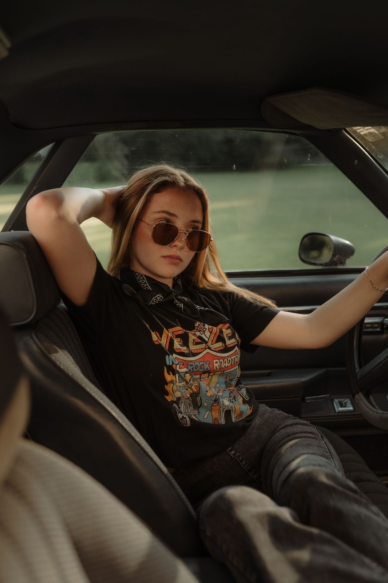 A person in a black t-shirt with orange graphics reclines in the driver's seat of a car.