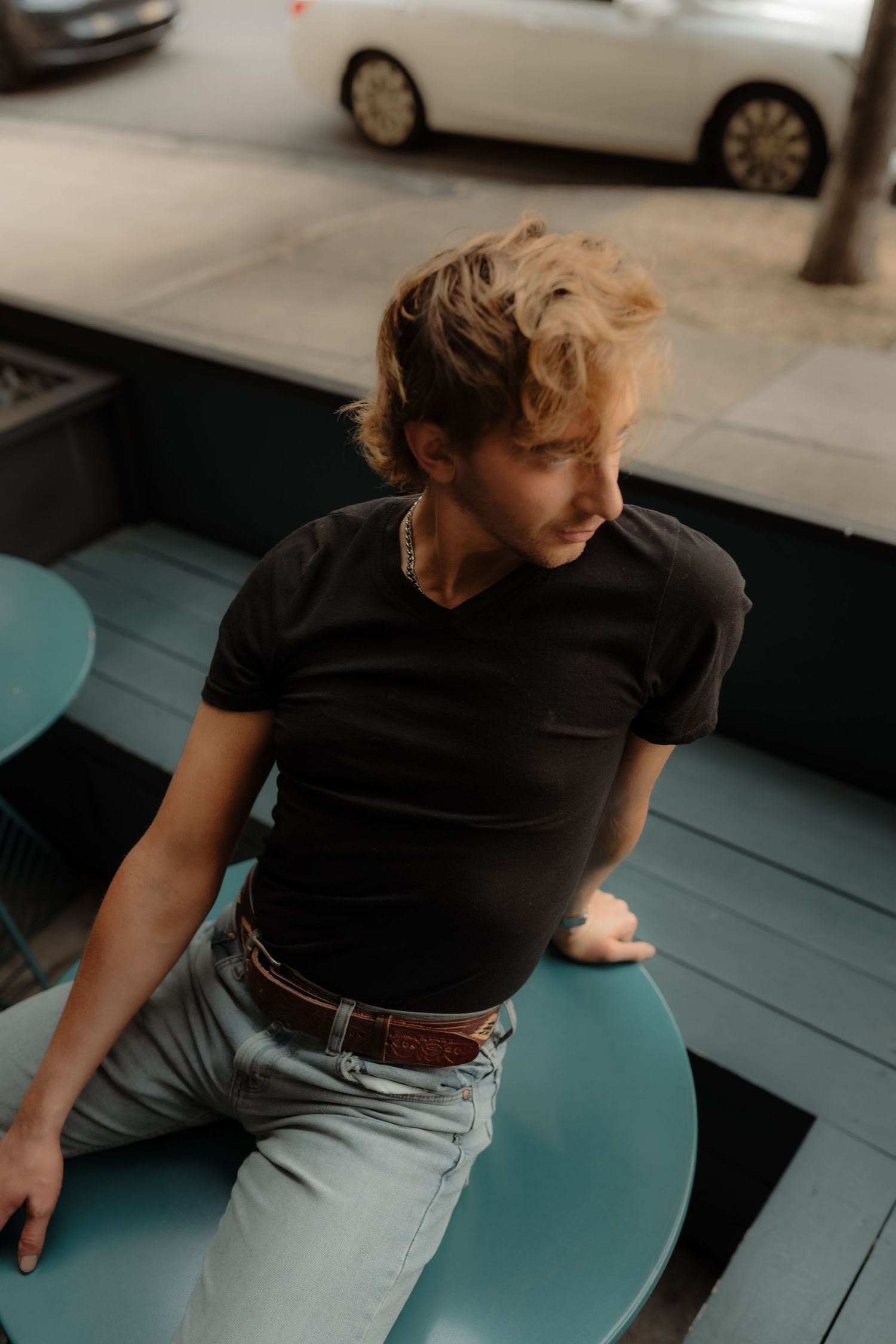 A person wearing a black t-shirt sits on a teal-colored surface in a sequence of candid poses.