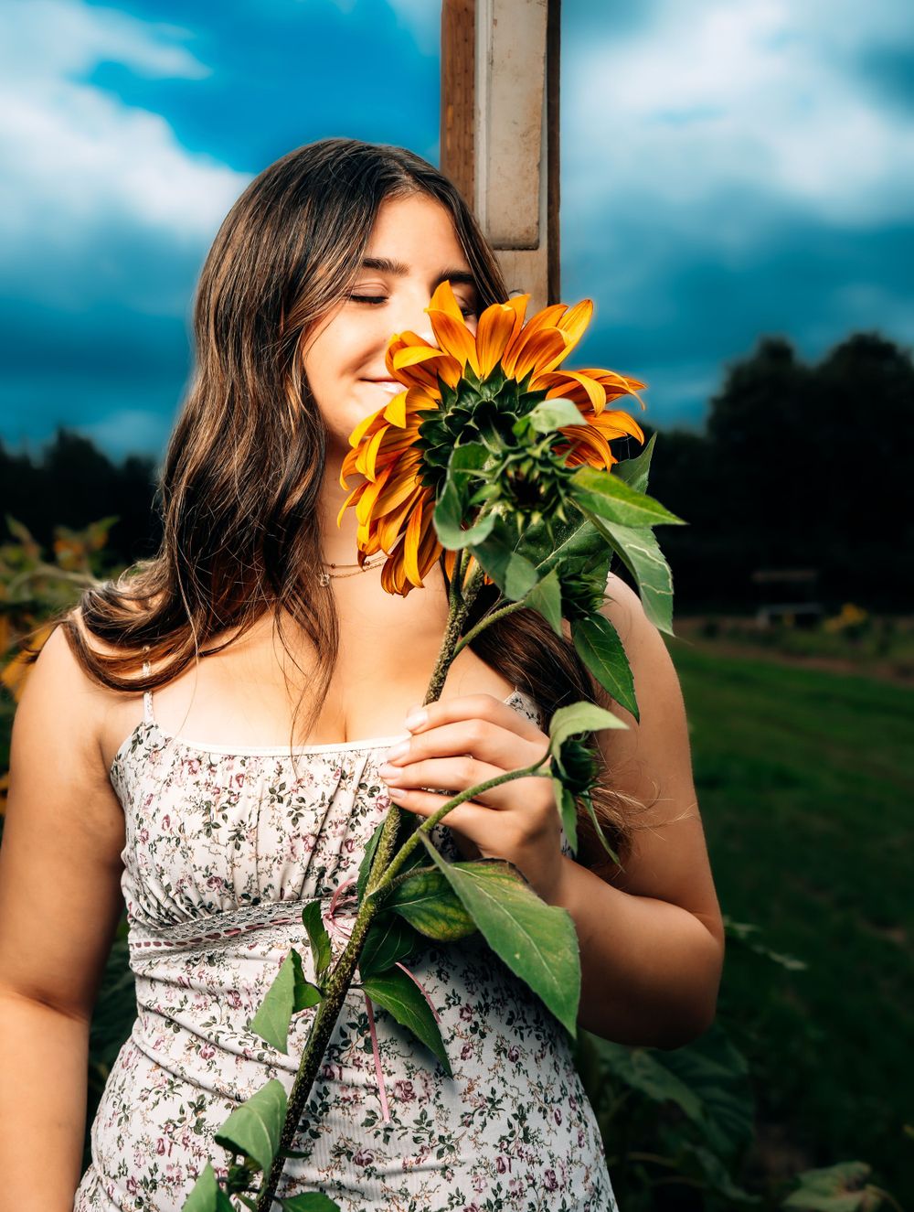 Candid floral portrait with sunflower and floral dress against moody sky.