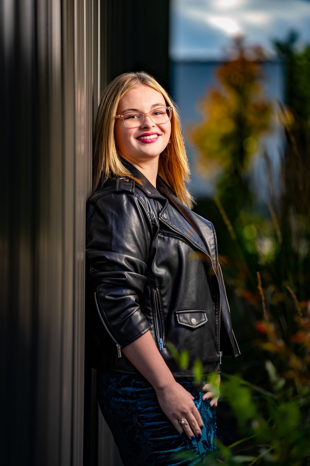 Fashion portrait with black leather jacket against architectural columns and foliage.