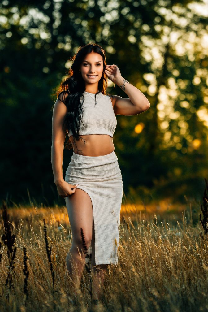 Golden hour portrait of someone in a cream-colored two-piece outfit standing in tall grass.