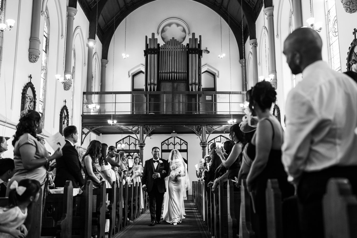 Bride and her father walk down the aisle in a church as wedding guests watch.