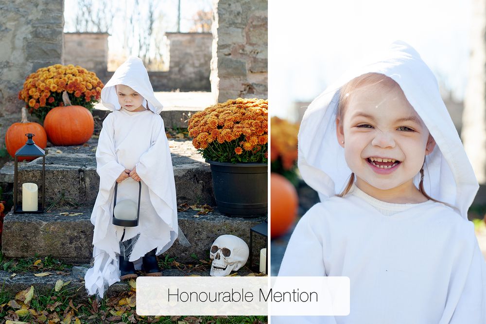 Child in a white ghost costume holding a lantern beside orange pumpkins, mums, and a skull on stone steps, with a smiling close-up portrait.