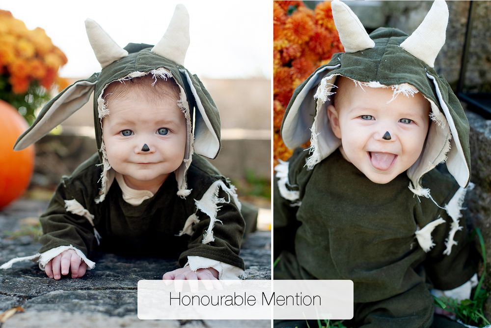 Baby in a green horned monster costume with a painted nose crawls and sticks out its tongue near autumn pumpkins and orange flowers.