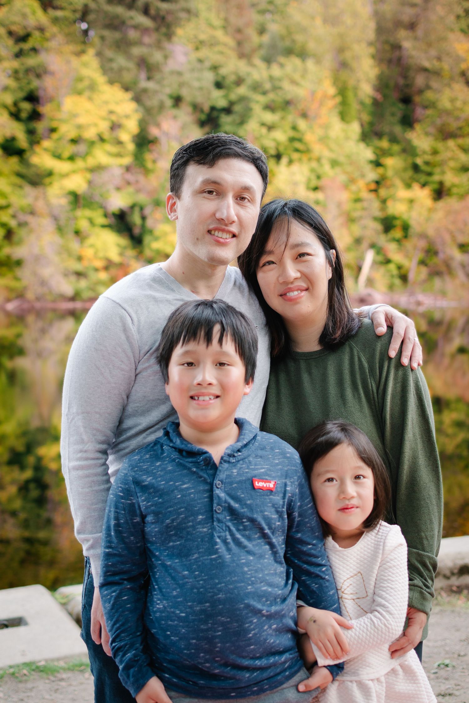 Family of four posing together outdoors with autumn foliage at Lake Fenwick Park