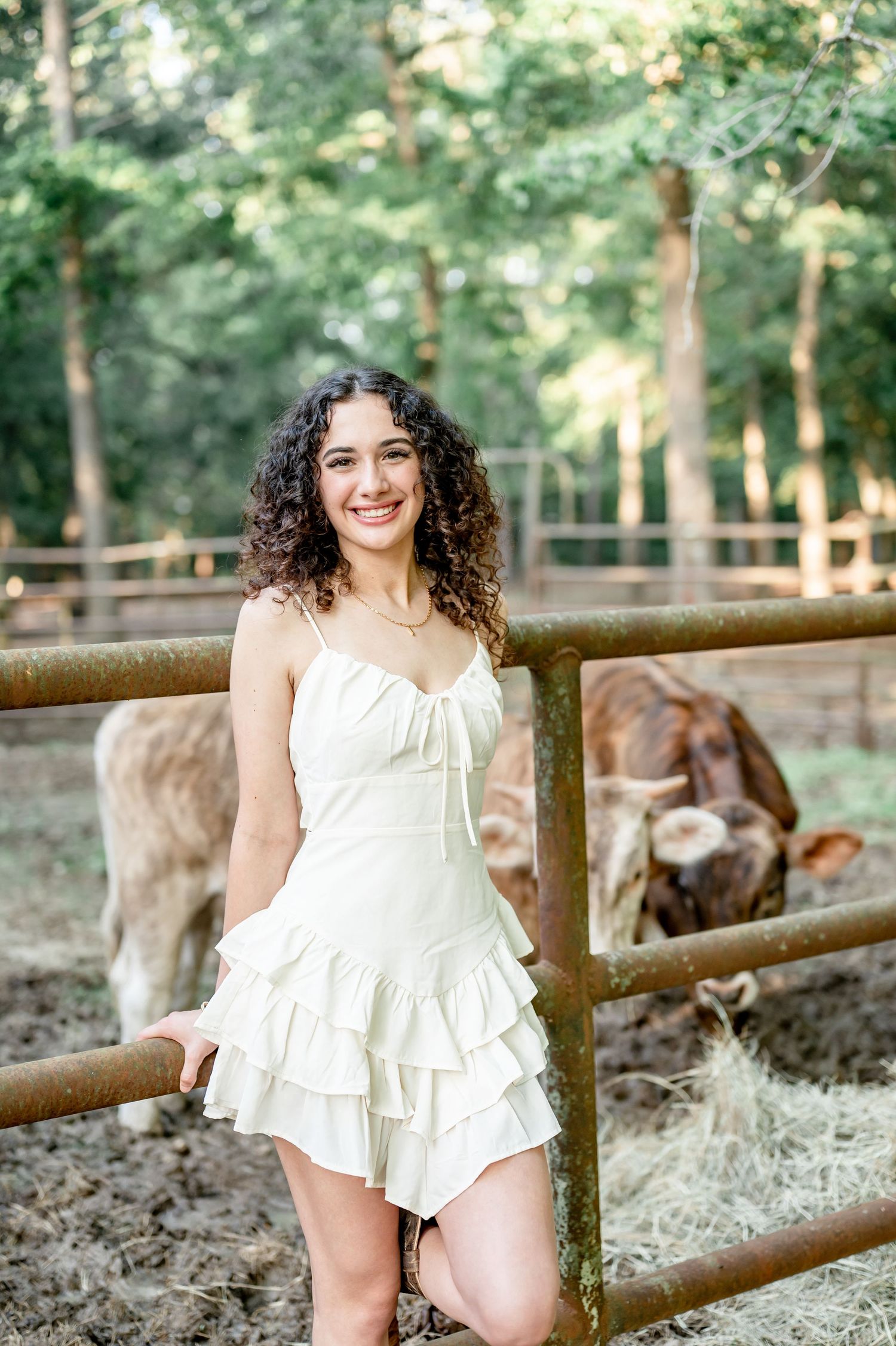 Young woman with curly hair in white dress poses gracefully outdoors in a sunlit park setting.