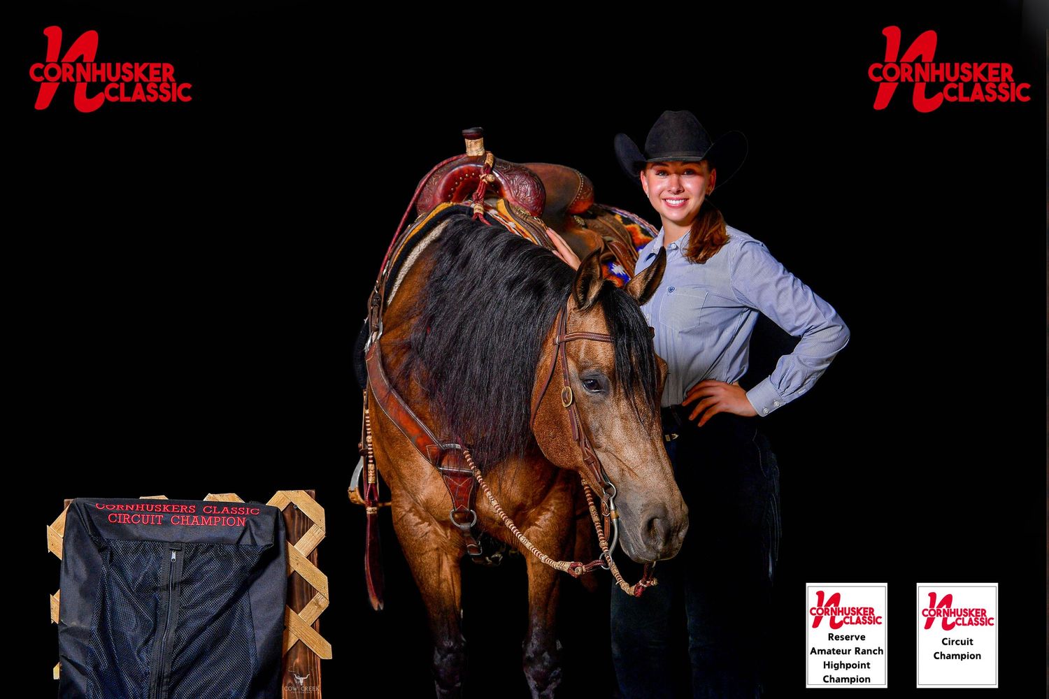 A rider in red western attire sits atop a chestnut horse surrounded by a group of people and a golden retriever at an equestrian show.