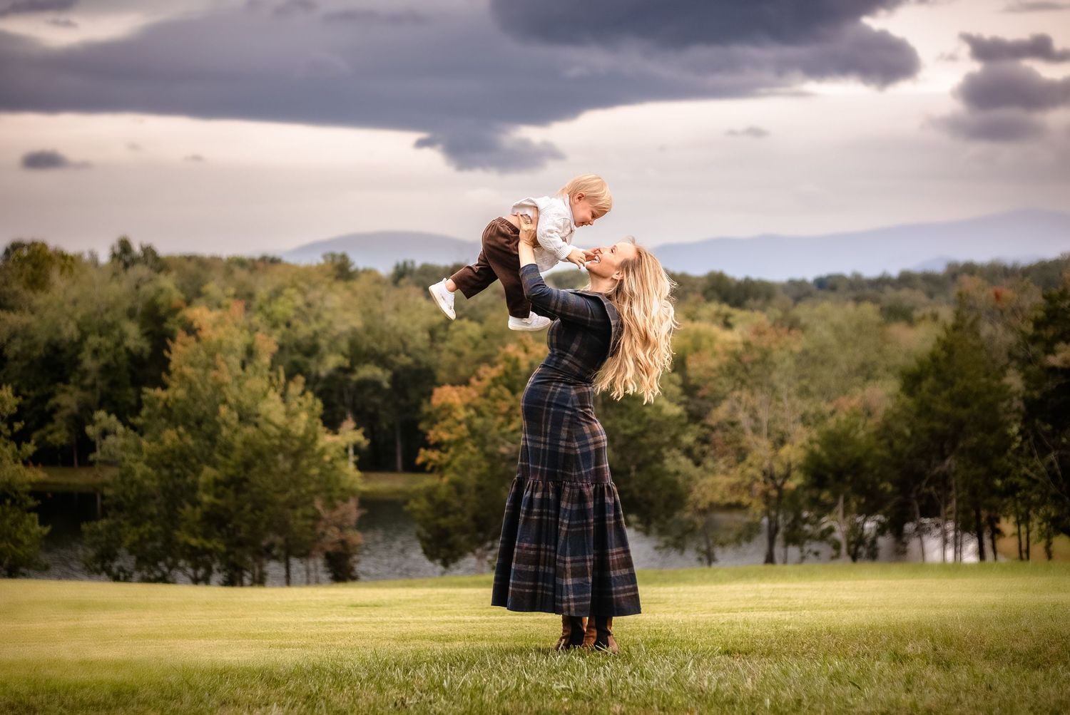 Gorgeous blond mama in plaid lifts her toddler son into the air against a fall mountain backdrop by Charlottesville family photographer.