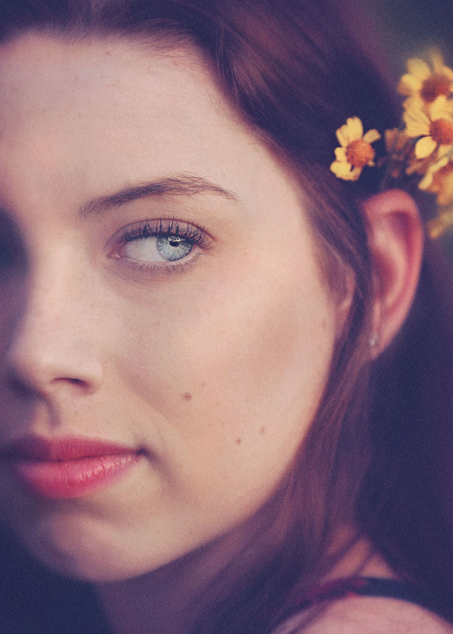 Close-up portrait of a woman with blue eyes, red lipstick and small yellow flowers tucked in her long auburn hair.