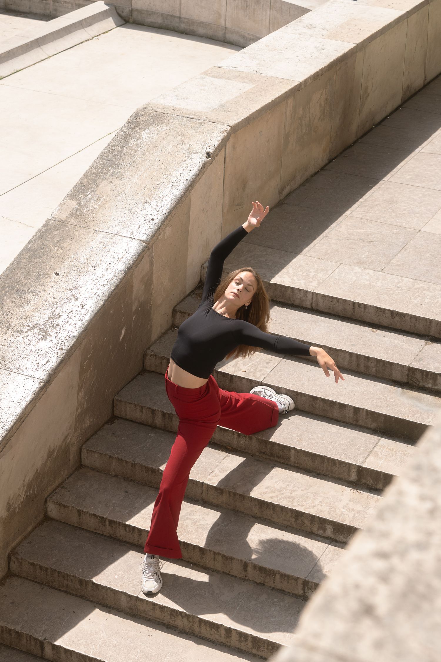 Danseuse en pantalon rouge, jambe levée, sur des escaliers en pierre