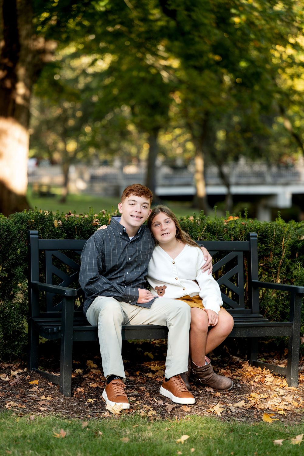 Teen boy and girl sit together on black park bench smiling in autumn garden setting.